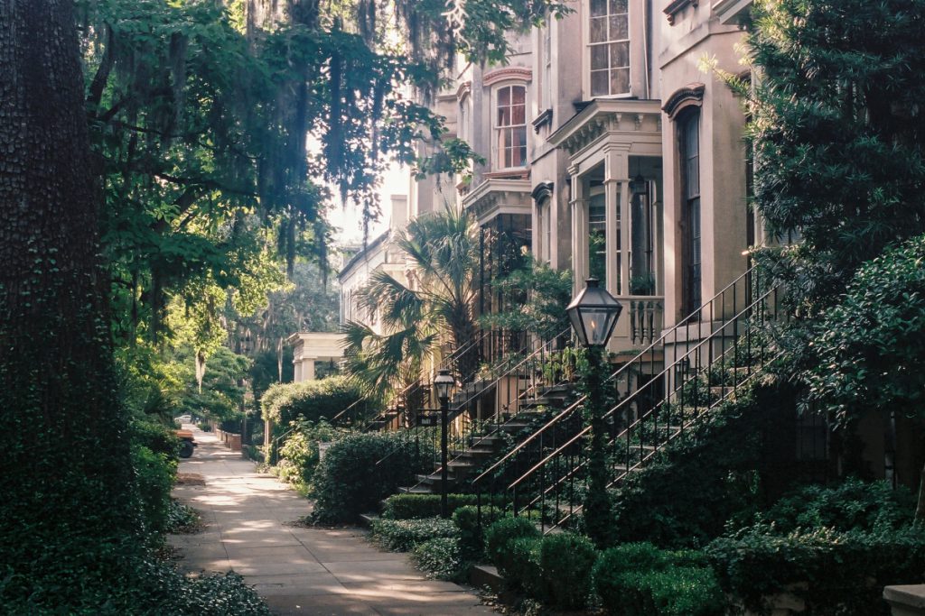 townhome facades surrounded by large green trees and shrubs lined with black street lights