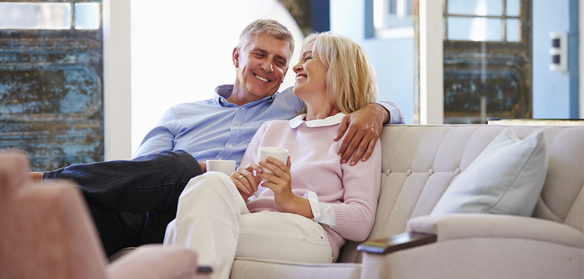 couple sitting on beige couch hugging and smiling holding mugs