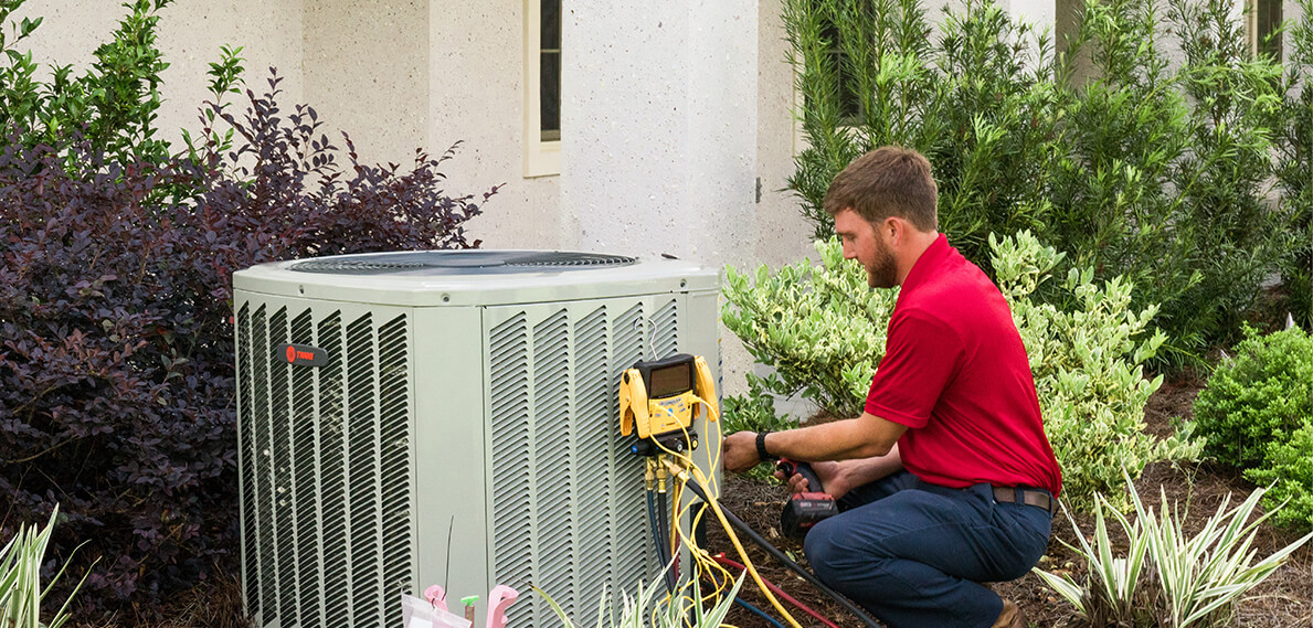 canady's technician conducting a maintenance check on hvac unit near greenery and stucco home