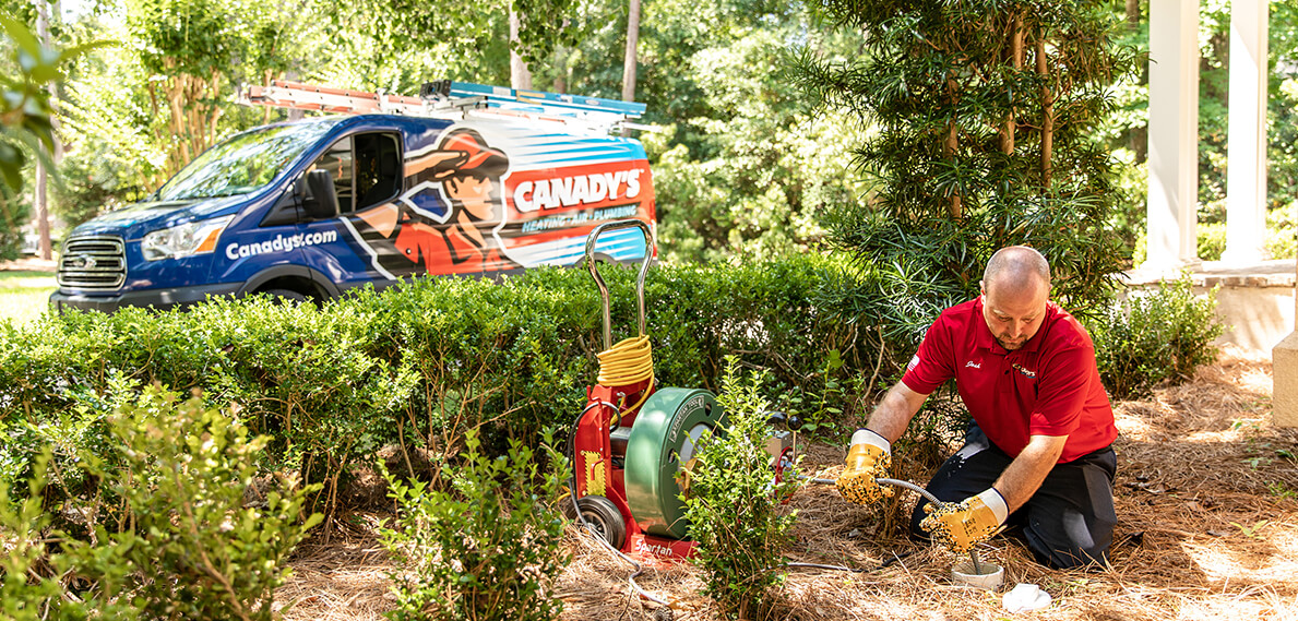 canady's technician in front yard wearing gloves clearing drain in front of service vehicle